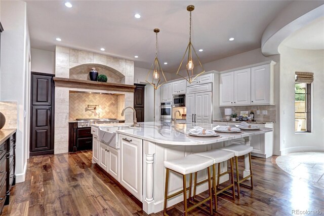 kitchen featuring white cabinets, oven, a large island with sink, dark wood-style floors, and tasteful backsplash