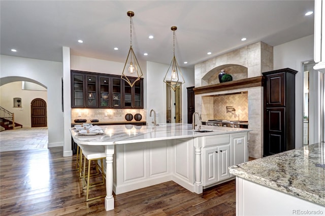 kitchen with decorative backsplash, arched walkways, dark wood-style flooring, and a sink