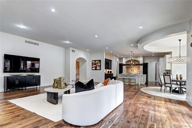 living room featuring light wood finished floors, visible vents, arched walkways, and recessed lighting