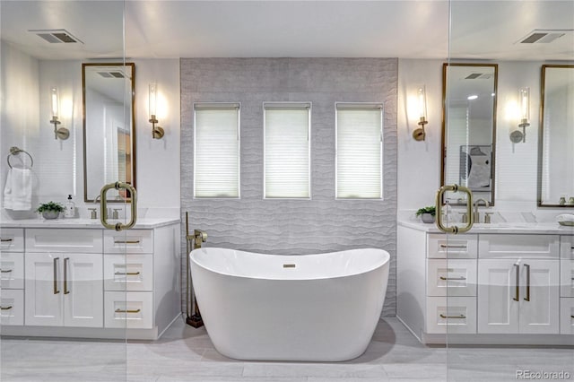 full bath with a soaking tub, two vanities, and visible vents