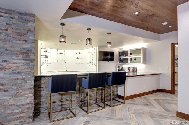 bar featuring baseboards, hanging light fixtures, wooden ceiling, and a sink