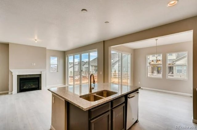 kitchen featuring light stone counters, stainless steel dishwasher, a glass covered fireplace, a sink, and dark brown cabinets