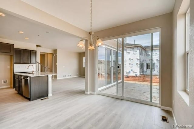 unfurnished dining area with light wood-style flooring, a sink, visible vents, baseboards, and an inviting chandelier