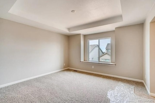 unfurnished room featuring carpet, a raised ceiling, and baseboards