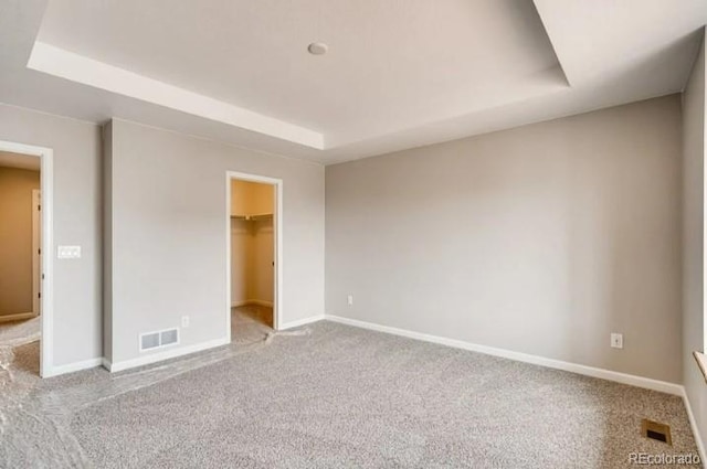 unfurnished bedroom featuring carpet, baseboards, visible vents, and a raised ceiling