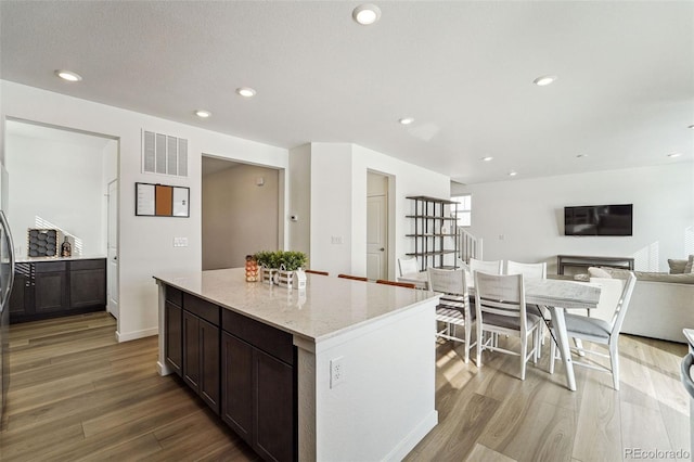 kitchen with light stone counters, light wood-type flooring, dark brown cabinetry, and a kitchen island