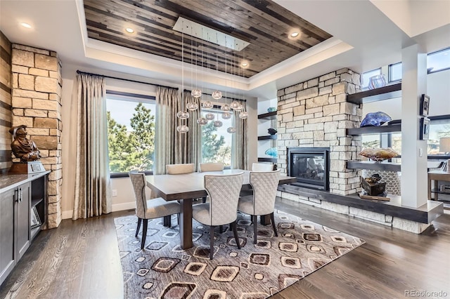 dining area featuring a raised ceiling, a stone fireplace, wood ceiling, and dark hardwood / wood-style floors