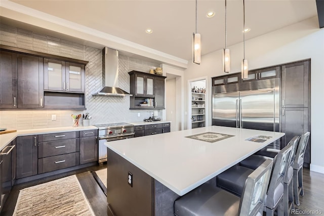 kitchen with wall chimney exhaust hood, pendant lighting, high quality appliances, a kitchen island, and dark brown cabinetry