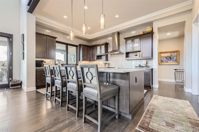 kitchen featuring a center island, a breakfast bar, pendant lighting, dark brown cabinets, and wall chimney range hood