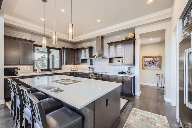 kitchen featuring dark brown cabinetry, wall chimney range hood, hanging light fixtures, and a center island