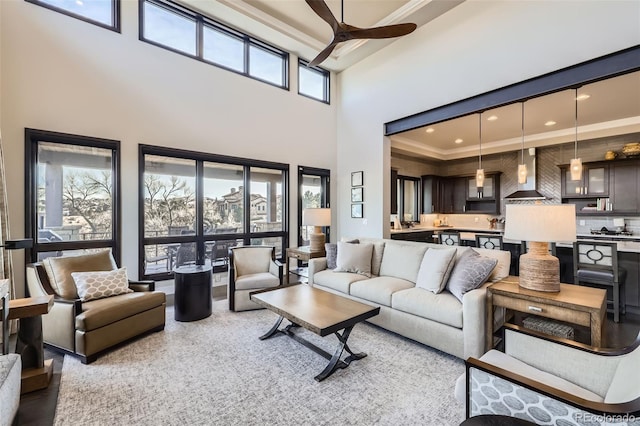 living room featuring ceiling fan, crown molding, a wealth of natural light, and a high ceiling