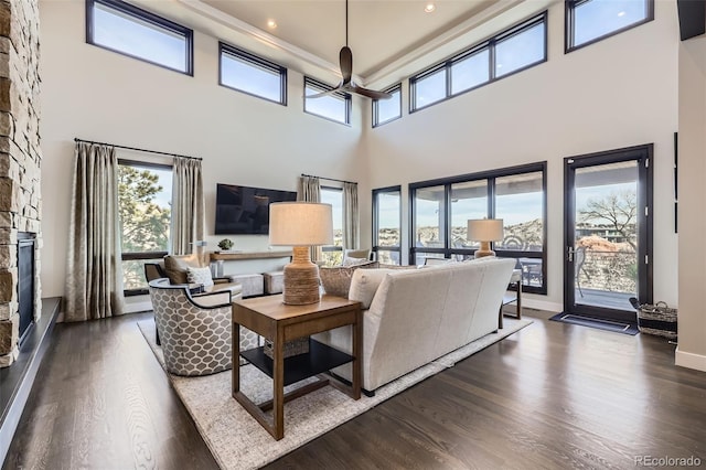 living room featuring a high ceiling, a stone fireplace, ceiling fan, and dark hardwood / wood-style floors