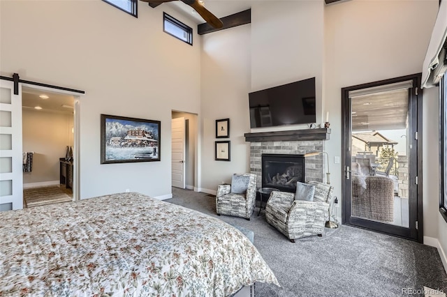 carpeted bedroom featuring a towering ceiling, access to exterior, ceiling fan, and a stone fireplace