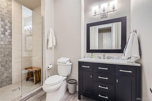 bathroom with toilet, hardwood / wood-style flooring, tiled shower, and vanity