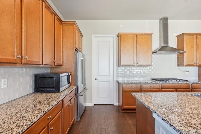 kitchen with light stone counters, dark hardwood / wood-style floors, wall chimney exhaust hood, decorative backsplash, and appliances with stainless steel finishes