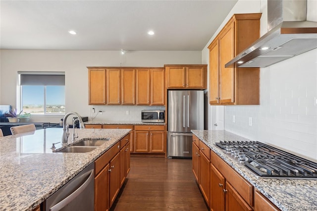 kitchen with light stone counters, sink, dark wood-type flooring, wall chimney range hood, and appliances with stainless steel finishes