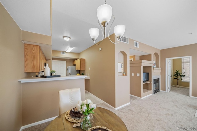 kitchen with a fireplace, stainless steel refrigerator, a chandelier, kitchen peninsula, and light carpet