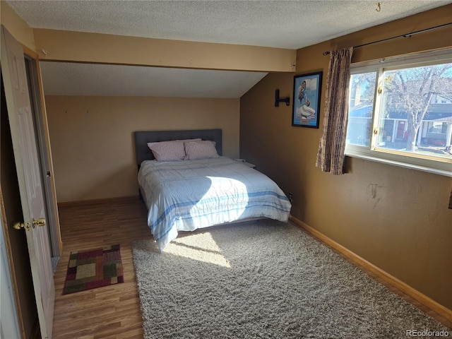 bedroom with a textured ceiling, wood-type flooring, and lofted ceiling