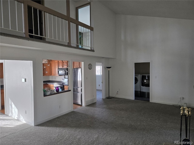 unfurnished living room featuring dark carpet, separate washer and dryer, and high vaulted ceiling