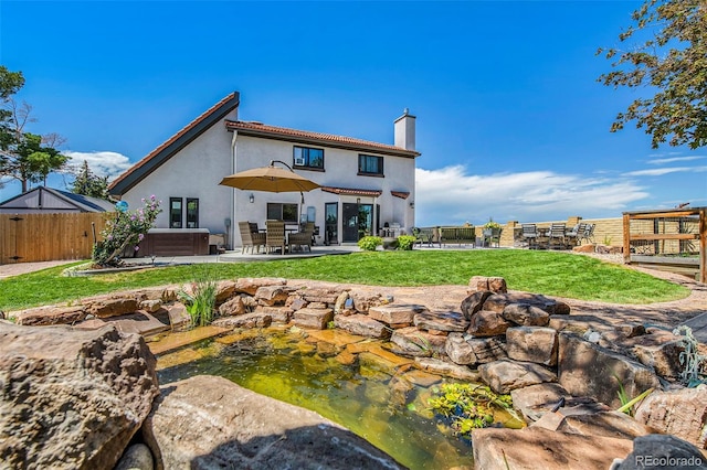 back of house featuring a hot tub, a patio area, and a lawn