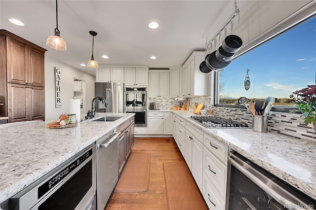 kitchen featuring stainless steel appliances, beverage cooler, sink, pendant lighting, and white cabinets