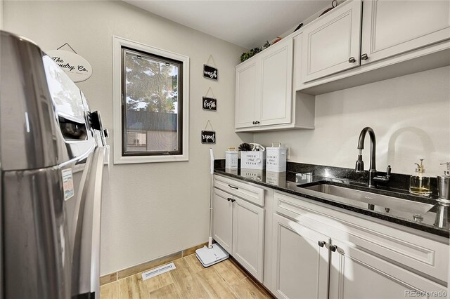 kitchen with white cabinets, stainless steel refrigerator with ice dispenser, dark stone countertops, and sink