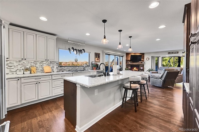 kitchen with white cabinets, a kitchen breakfast bar, a center island with sink, sink, and dark hardwood / wood-style flooring