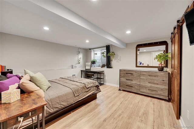 bedroom with a barn door and light hardwood / wood-style floors