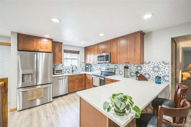 10462 Hoyt St, Westminster, CO 80021 - kitchen with appliances with stainless steel finishes, light countertops, a peninsula, light wood-style flooring, and brown cabinetry