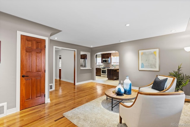 living area with light wood-style floors, arched walkways, baseboards, and recessed lighting