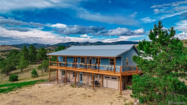 rear view of property featuring driveway, a garage, stone siding, metal roof, and a deck with mountain view