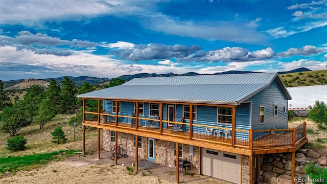 rear view of house featuring a garage, stone siding, a deck with mountain view, and metal roof