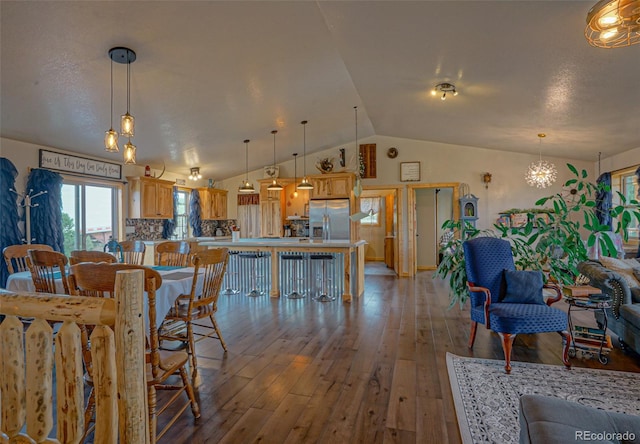 dining space featuring a notable chandelier, wood-type flooring, and vaulted ceiling