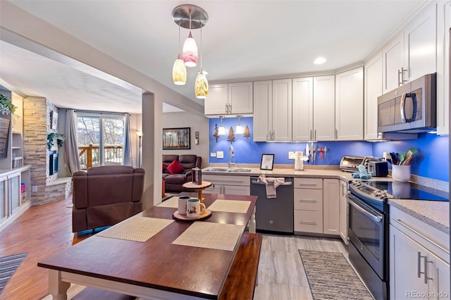 kitchen with white cabinetry, stainless steel appliances, decorative light fixtures, light hardwood / wood-style flooring, and sink