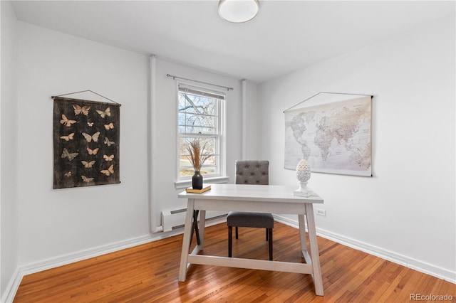 office space with a baseboard heating unit, baseboards, and light wood-type flooring