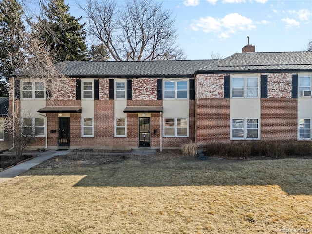 view of property with brick siding, a chimney, and a front lawn