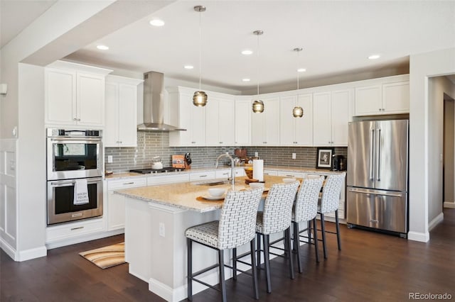 kitchen with a sink, dark wood finished floors, appliances with stainless steel finishes, a breakfast bar area, and wall chimney range hood