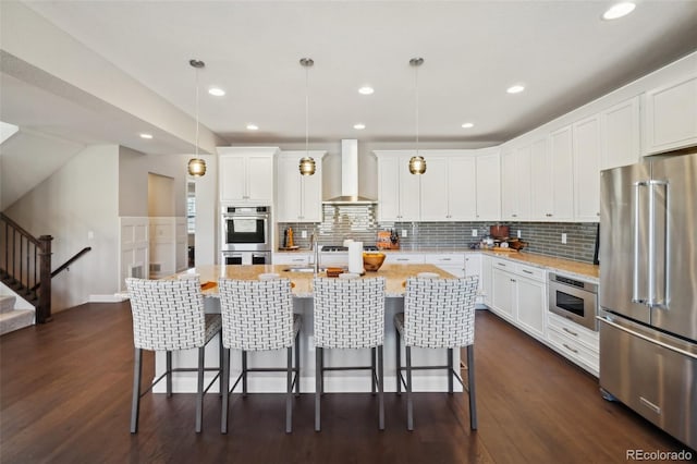 kitchen featuring white cabinets, appliances with stainless steel finishes, wall chimney exhaust hood, and dark wood-style flooring