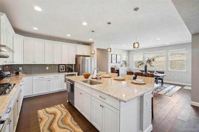 kitchen with a center island with sink, a sink, backsplash, white cabinetry, and appliances with stainless steel finishes