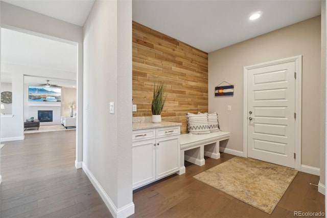 mudroom with a glass covered fireplace, baseboards, wooden walls, and dark wood finished floors