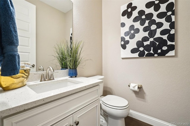 bathroom featuring vanity, toilet, a textured wall, and baseboards