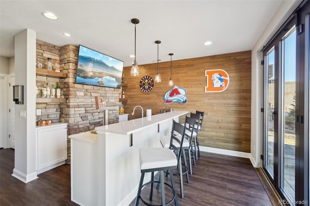 bar with dark wood finished floors, wood walls, and hanging light fixtures