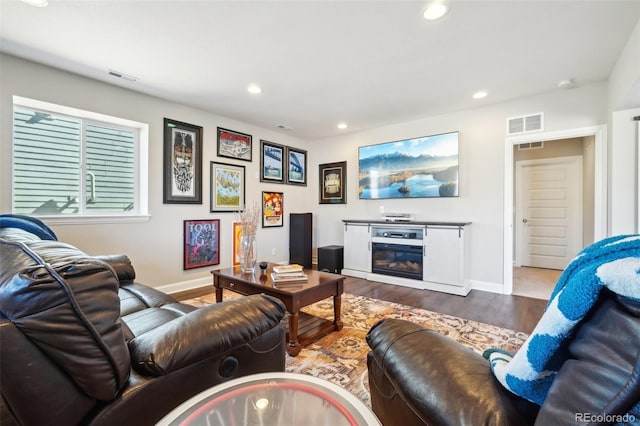 living area with a glass covered fireplace, wood finished floors, recessed lighting, and visible vents