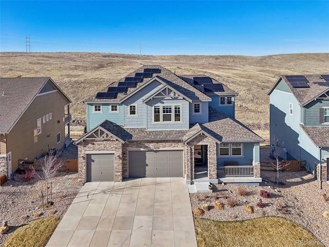 view of front of house with driveway, stone siding, roof mounted solar panels, a porch, and an attached garage