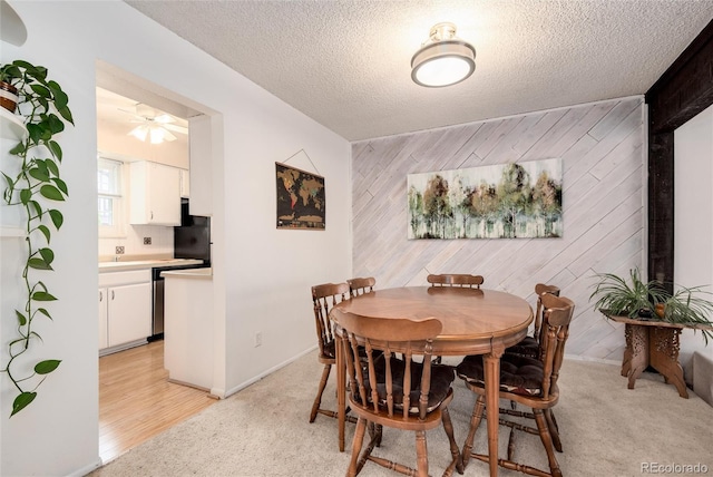 dining room with light colored carpet, a textured ceiling, and wood walls