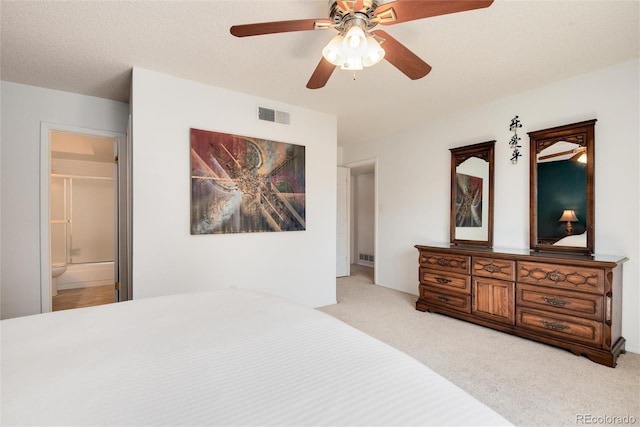 bedroom featuring ceiling fan, ensuite bath, light colored carpet, and a textured ceiling