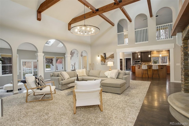 living room featuring beamed ceiling, high vaulted ceiling, an inviting chandelier, and ornate columns