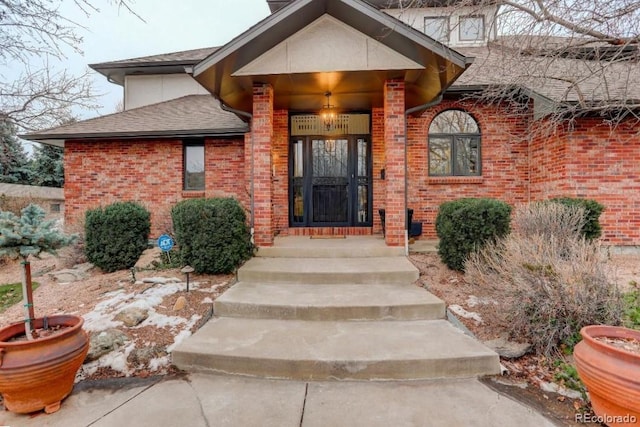 view of exterior entry with brick siding and roof with shingles