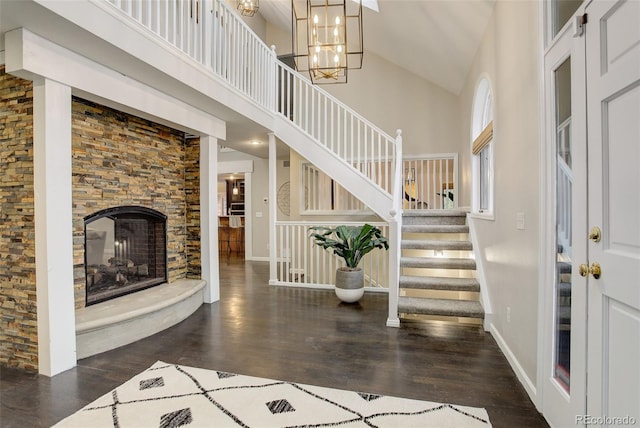 foyer entrance with baseboards, dark wood-style floors, a high ceiling, a stone fireplace, and a chandelier