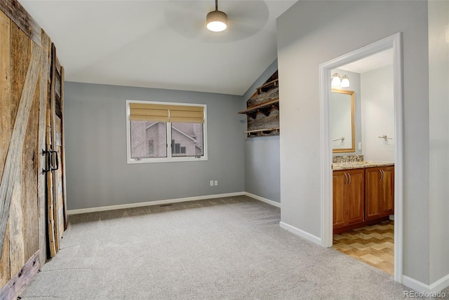 unfurnished bedroom featuring ceiling fan, connected bathroom, light carpet, baseboards, and vaulted ceiling